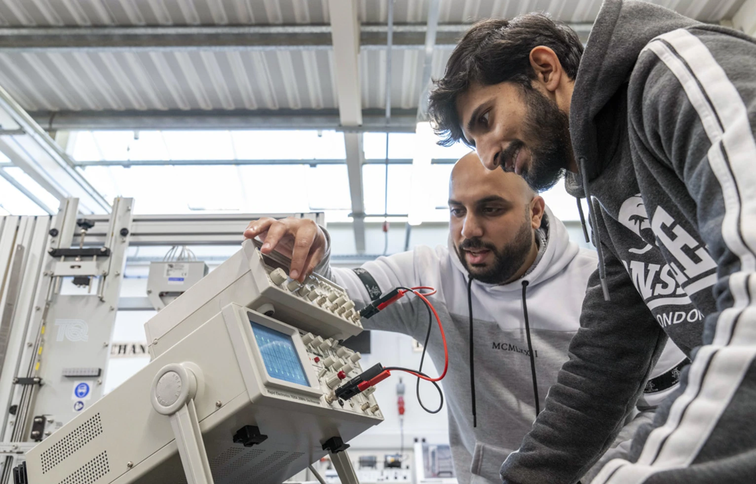 Two students working together on an oscilloscope, adjusting settings to analyze waveforms in an electronics engineering lab. Two students working together on an oscilloscope, adjusting settings to analyze waveforms in an electronics engineering lab.